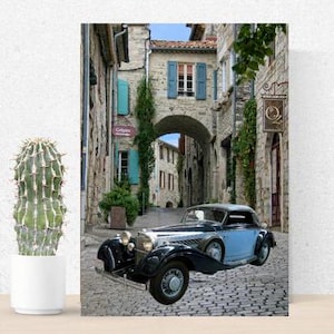 Op de afbeelding: Een vintage blauwe en zwarte cabriolet geparkeerd in een smalle geplaveide straat in een Europees dorp. De auto staat geparkeerd onder een boog met stenen gebouwen aan beide kanten.