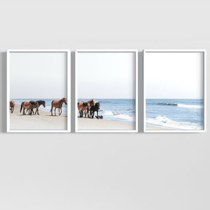 May include: Triptych of framed art prints featuring wild horses on a sandy beach. The horses, in shades of brown and black, are near the water's edge. The ocean and sky are a soft blue, creating a serene coastal scene.