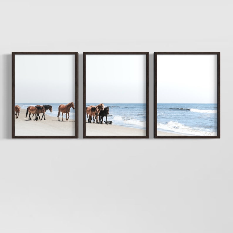 May include: Set of three framed prints featuring horses on a beach. The horses, in shades of brown and black, are depicted near the ocean's edge. The sky is a pale blue, and the frames are dark brown.