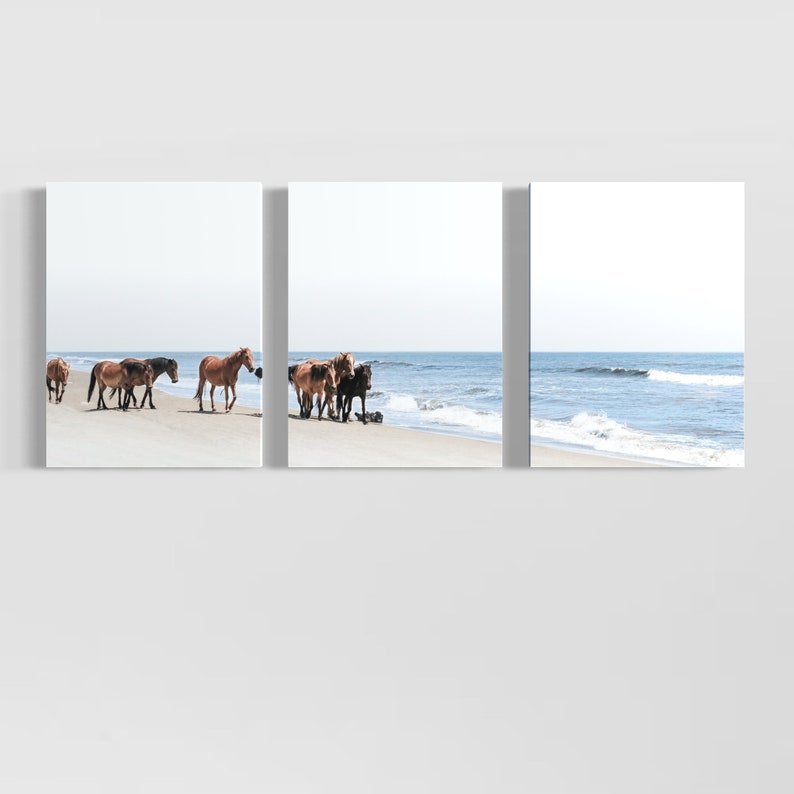 May include: A triptych canvas print featuring wild horses on a sandy beach. The horses, in shades of brown and black, are near the water's edge. The ocean and sky are a light blue.