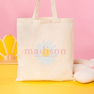 Pode incluir: Uma bolsa tote branca com um desenho de margarida e o texto "madison daisy troop #476".