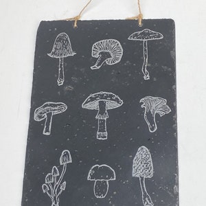 May include: A black slate sign with a string hanger features a white outline of various mushroom illustrations.