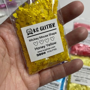 May include: A small clear plastic bag filled with yellow glitter shaped like Mickey Mouse heads. The bag has a white label that reads "KC GLITTER Mickey Mouse Shape Honey Yellow www.kcglitter.com KCGlitter".