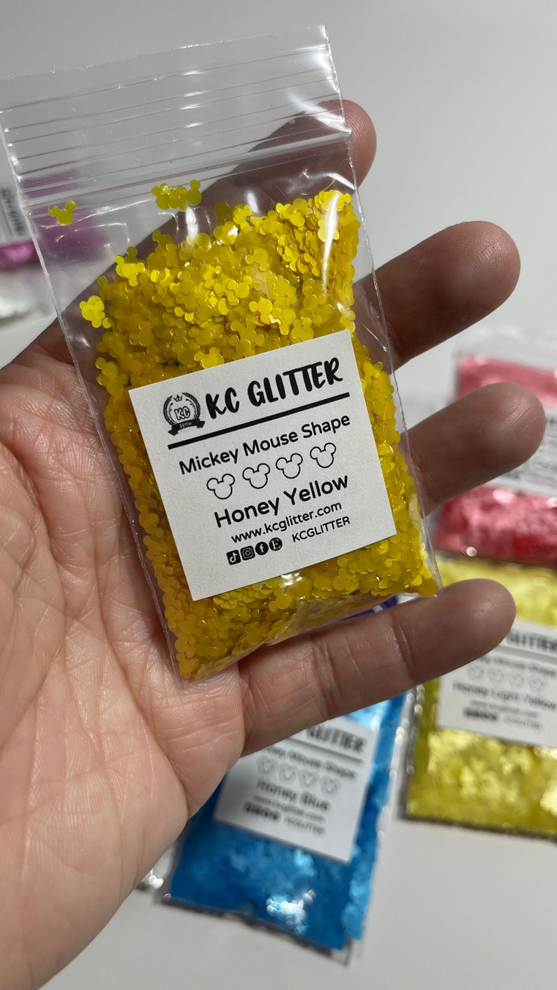 May include: A small clear plastic bag filled with yellow glitter shaped like Mickey Mouse heads. The bag has a white label that reads "KC GLITTER Mickey Mouse Shape Honey Yellow www.kcglitter.com KCGlitter".