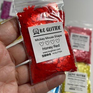 May include: A small plastic bag filled with red glitter shaped like Mickey Mouse heads. The bag has a label that reads "KC GLITTER Mickey Mouse Shape Honey Red www.kcglitter.com KCGlitter".