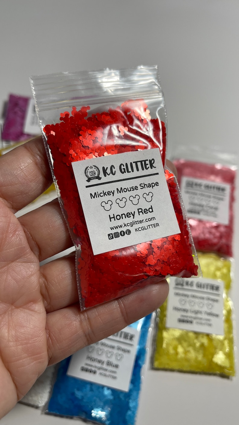 May include: A small plastic bag filled with red glitter shaped like Mickey Mouse heads. The bag has a label that reads "KC GLITTER Mickey Mouse Shape Honey Red www.kcglitter.com KCGlitter".