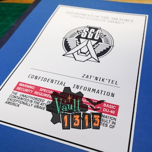 May include: A blue folder with a white document featuring the text "DEPARTMENT OF THE AIR FORCE UNITED STATES OF AMERICA" and "CONFIDENTIAL INFORMATION". The document has a logo and the text "ZAT'NIK'TEL". A red warning label is visible.