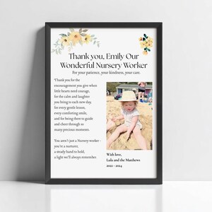 May include: A framed print with a black border. The print features text that reads "Thank you, Emily Our Wonderful Nursery Worker" with a photo of a child. Floral accents in yellow and white are at the top.