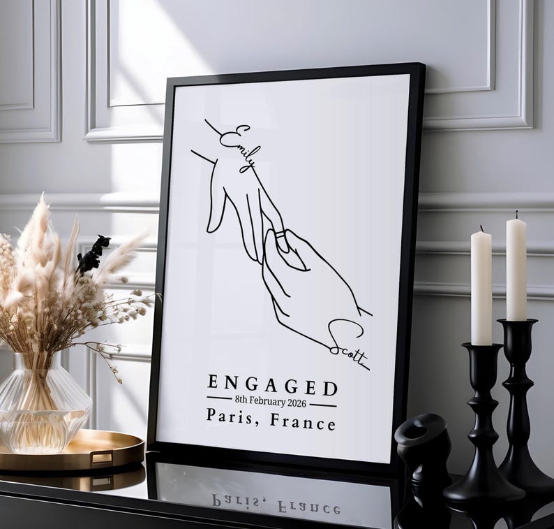 Minimalist line art print of two hands with an engagement ring, personalised with couple's names in handwritten script and custom engagement date and location beneath.