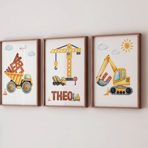 May include: Three watercolour illustrations of construction vehicles, including a dumper truck, a crane, and an excavator. The illustrations are framed in wood and feature the name "THEO" in brick-like letters.