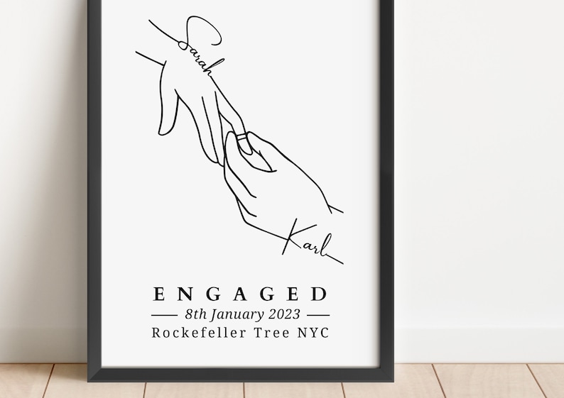 May include: Black and white line art print featuring two hands, one placing a ring on the other. The names "Sarah" and "Karl" are written on the hands. The word "ENGAGED" and the date "8th January 2023" are also included.