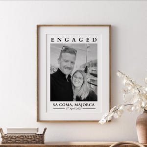 May include: Black and white photo of a couple engaged in Sa Coma, Majorca on April 5th, 2025. The couple is standing in front of a body of water with boats in the background.
