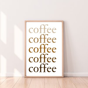 Könnte beinhalten: Ein gerahmter Druck mit dem Wort "coffee" fünfmal in verschiedenen Brauntönen wiederholt. Der Text befindet sich auf weißem Hintergrund, in einem hellbraunen Holzrahmen. Der Druck wird vor einer weißen Wand und einem Holzboden präsentiert.