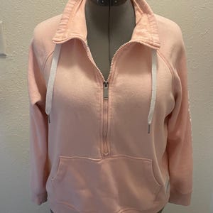 May include: A pink quarter-zip sweatshirt with a white drawstring and a kangaroo pocket.