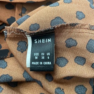 May include: Close-up of a brown fabric with black polka dots. The tag reads "SHEIN" with size information: M, EU 38, US 6. The tag also states "MADE IN CHINA".