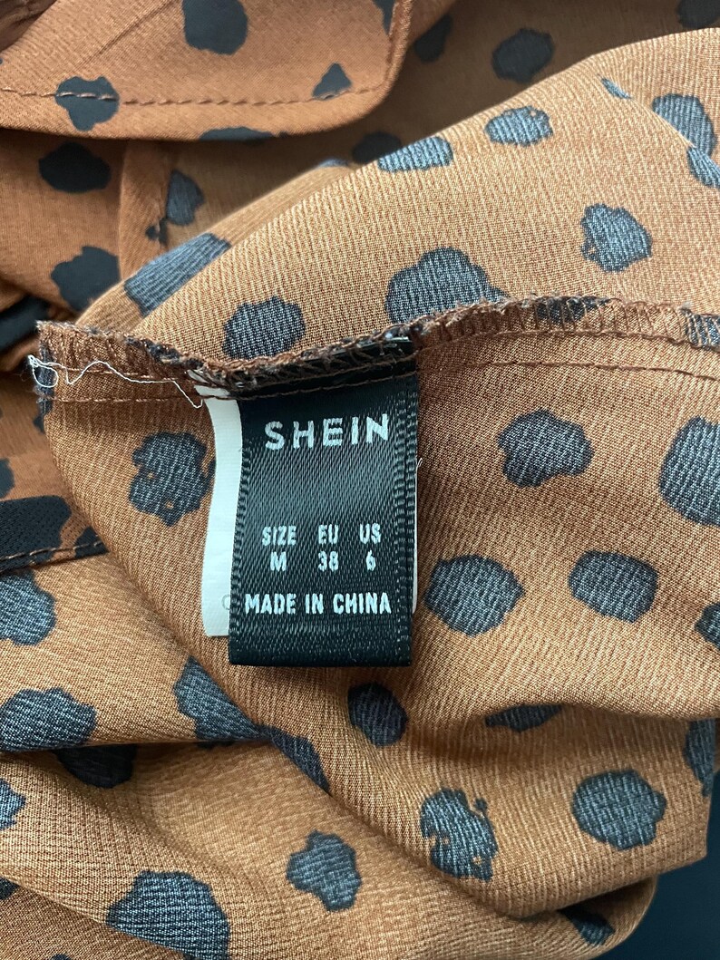 May include: Close-up of a brown fabric with black polka dots. The tag reads "SHEIN" with size information: M, EU 38, US 6. The tag also states "MADE IN CHINA".