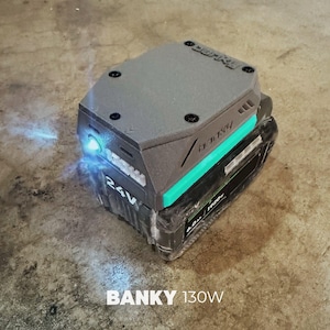 Puede incluir: Accesorio para herramienta eléctrica gris y negro con un acento turquesa, con el texto "BANKY 130W" y "24V". El accesorio tiene una luz incorporada y está diseñado para colocarse encima de una batería negra.