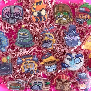 May include: A collection of 16 colorful cartoon character pins. The pins are made of clear acrylic and feature a variety of characters, including a robot, a ghost, a monster, and a knight. The pins are perfect for adding a touch of whimsy to your backpack, jacket, or hat.