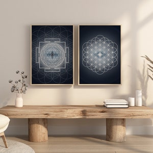 May include: Two framed wall art prints with geometric designs. One features a Sri Yantra, the other a Flower of Life pattern, both in white on a dark blue background. The frames are a light wood color.