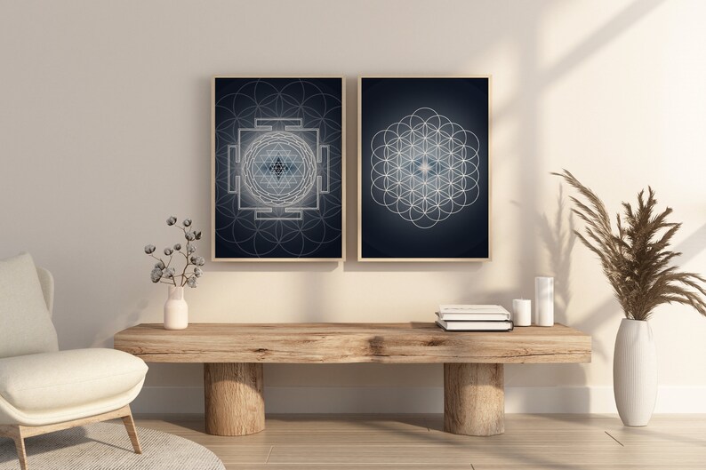 May include: Two framed wall art prints with geometric designs. One features a Sri Yantra, the other a Flower of Life pattern, both in white on a dark blue background. The frames are a light wood color.