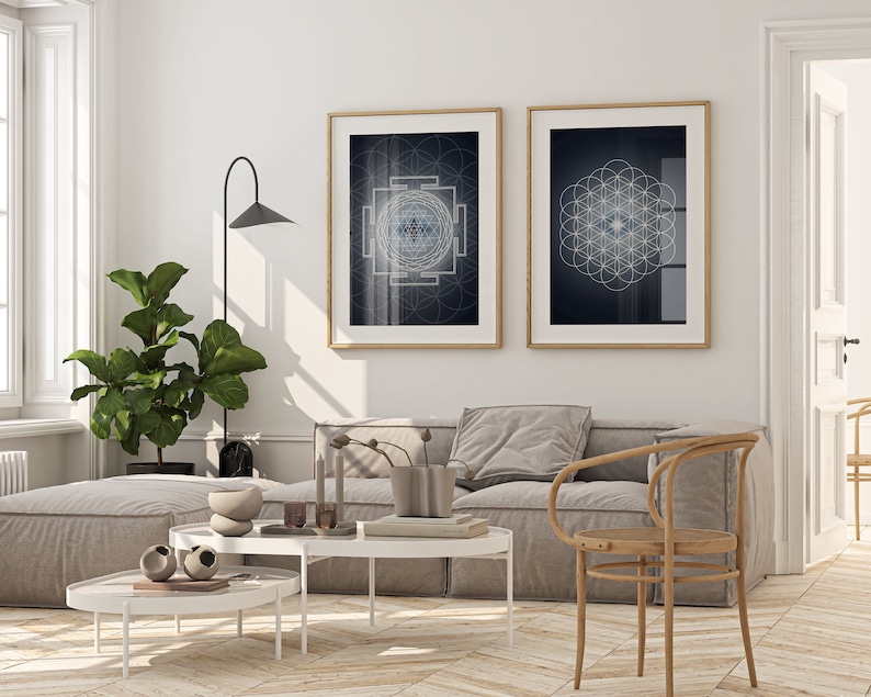 May include: Two framed wall art prints with geometric designs hang above a gray sofa. The prints have gold frames and feature intricate patterns in shades of blue and white against a dark background. The room is decorated with a large potted plant and a modern lamp.