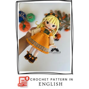 Op de afbeelding: Handgemaakte gehaakte pop met blond haar, gekleed in een oranje jurk en bruine schoenen. De pop heeft een groen en bruin lijfje en een bijpassende haarband. De tekst "CROCHET PATTERN IN ENGLISH" is inbegrepen.
