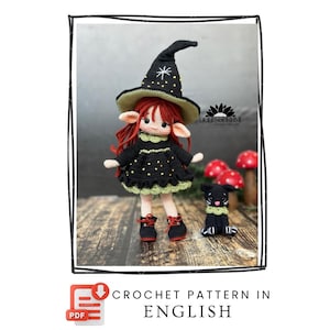 May include: A crochet doll with red hair, wearing a black witch hat with yellow stars and a black dress with a green scalloped hem. The doll has pointed ears and wears black shoes with red laces. Beside the doll is a small black crochet cat.