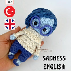 May include: Crochet pattern for a blue and white amigurumi doll with glasses, titled "Sadness English Pattern".