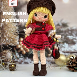 Może przedstawiać: Wzór na szydełkową lalkę w formacie PDF. Lalka ma na sobie czerwoną sukienkę z brązowymi lamówkami, brązowy kapelusz i brązowe buty. Trzyma książkę i małą brązową torebkę.
