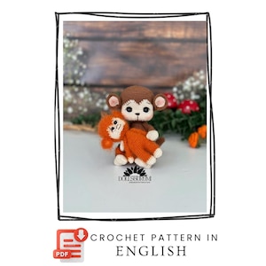 Puede incluir: Dos muñecos de mono de ganchillo, uno marrón y otro naranja, se muestran. El mono marrón está abrazando al mono naranja. El texto "CROCHET PATTERN IN ENGLISH" es visible. El fondo es una superficie de madera borrosa.