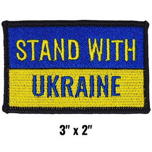 May include: Embroidered patch with the text "STAND WITH UKRAINE" in yellow and blue, mirroring the Ukrainian flag. The patch measures 3 inches by 2 inches and has a black border.