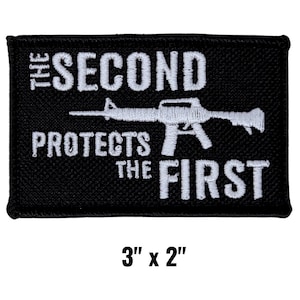 May include: Black rectangular patch with white embroidered text and a rifle graphic. The text reads "THE SECOND PROTECTS THE FIRST." The patch measures 3 inches by 2 inches.