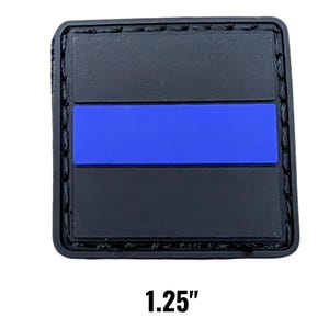 May include: A black square patch with a blue stripe across the center. The patch is 1.25 inches wide and has a stitched border. The design is simple and bold, with a focus on the contrasting colors.