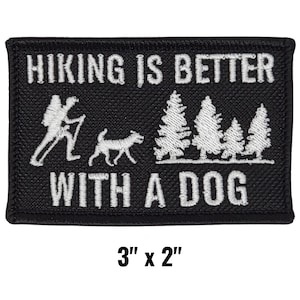 May include: Black rectangular patch with white embroidered text and graphics. The text reads "HIKING IS BETTER WITH A DOG." Graphics include a hiker, a dog, and pine trees. The patch measures 3 inches by 2 inches.