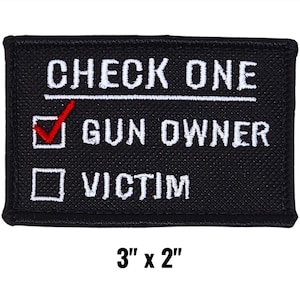 May include: Black rectangular patch with white text that reads "CHECK ONE" above two boxes. The first box is checked with a red checkmark and reads "GUN OWNER." The second box reads "VICTIM." The patch measures 3" x 2".