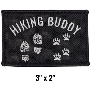 May include: Black rectangular patch with white embroidered text "HIKING BUDDY", footprints, and paw prints. The patch measures 3 inches by 2 inches.