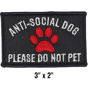 May include: A black rectangular patch with white text that reads "ANTI-SOCIAL DOG PLEASE DO NOT PET." A red paw print is centered below the words "ANTI-SOCIAL". The patch measures 3 inches by 2 inches.