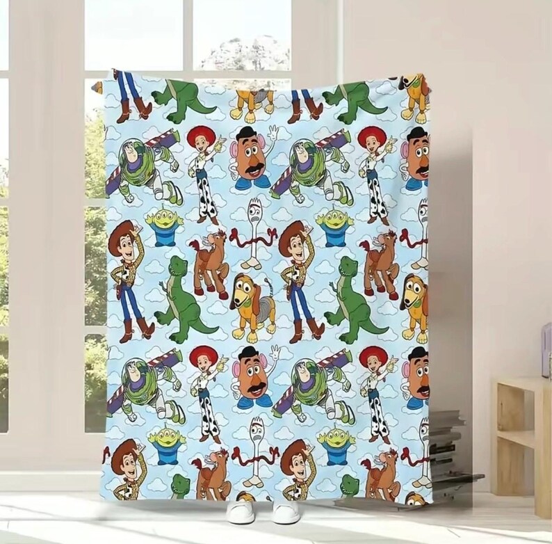 May include: A light blue fleece blanket featuring a repeating pattern of Toy Story characters including Woody, Buzz Lightyear, Jessie, Rex, Slinky Dog, Mr. Potato Head, Forky, and the green aliens against a backdrop of white clouds.