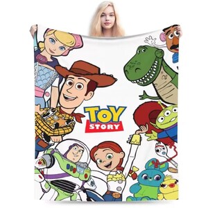 May include: A white fleece blanket featuring a colorful graphic print of Toy Story characters including Woody, Buzz Lightyear, Jessie, Bo Peep, Rex, Mr. Potato Head, the green aliens, Forky, Ducky, and Bunny, with the Toy Story logo in the center.