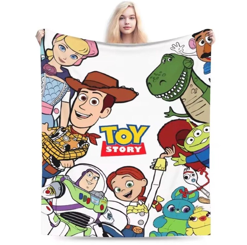 May include: A white fleece blanket featuring a colorful graphic print of Toy Story characters including Woody, Buzz Lightyear, Jessie, Bo Peep, Rex, Mr. Potato Head, the green aliens, Forky, Ducky, and Bunny, with the Toy Story logo in the center.