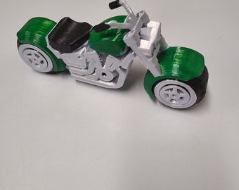 May include: A 3D-printed toy motorcycle in green, black, and white. The motorcycle features a detailed design with visible mechanical components, a black seat, and white wheels. The fenders and fuel tank are green.