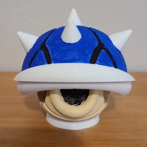 May include: A blue and white 3D printed model of a character from a video game. The character has a blue shell with white spikes and a white underside. The character is standing on a white base.