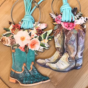 May include: Two wooden boot ornaments with floral accents and turquoise blue suede ties. The boots are decorated with watercolor-style floral designs and have a rustic charm.