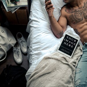 May include: A man lying in bed with a tablet displaying the text "YOUR IMAGE HERE". The tablet is on a white blanket. The man has tattoos on his chest and arms. He is wearing blue jeans and white underwear.
