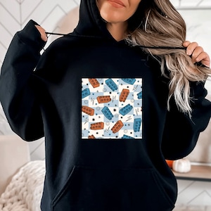 May include: Black hoodie with a pocket and a colorful graphic print of blue and orange building blocks on a white background. The graphic print is centered on the chest of the hoodie.