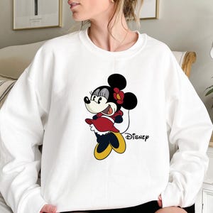 May include: White sweatshirt with a cartoon image of Minnie Mouse in a red dress and the word "Disney" printed on the front.