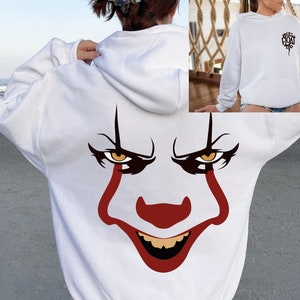 May include: White hoodie featuring a large graphic of a clown face on the back, with red, brown, and yellow details. The front of the hoodie has the text "You'll Float Too" in black. A hooded sweatshirt.