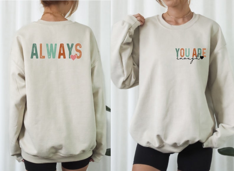 Może przedstawiać: Kremowa bluza z napisem "ALWAYS" w kolorowych literach z tyłu i r&oacute;żowym sercem. Prz&oacute;d bluzy ma napis "YOU ARE enough" w kolorze czarnym z małym czarnym sercem.