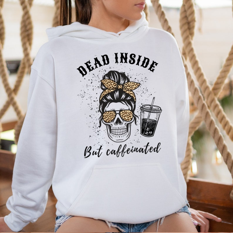 May include: White hoodie with a graphic of a skull wearing leopard print sunglasses and a matching headband. The text reads "DEAD INSIDE" above the skull and "But caffeinated" below. A cup of coffee is next to the skull.