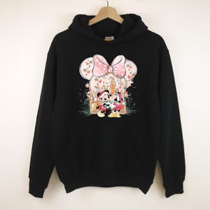 Peut inclure: Sweat-shirt &agrave; capuche noir avec un motif de Minnie et Mickey Mouse en tenue de f&ecirc;te. Le design comprend un n&oelig;ud rose, des motifs floraux et une sc&egrave;ne de vacances. Le sweat-shirt a une poche avant et une capuche &agrave; cordon.
